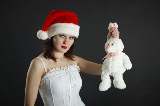 The woman in a Christmas cap holds in a hand a white rabbit on black