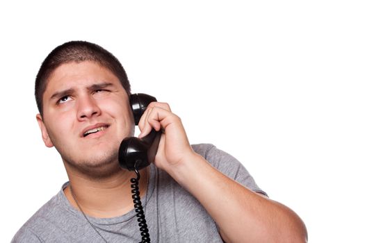 A young man listens on the telephone with an annoyed expression on his face.