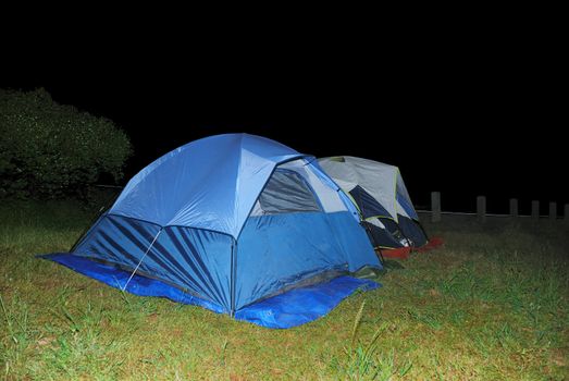 Two blue tents on green grass at night.