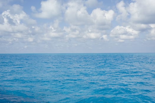 Landscape oriented background image of blue ocean water with a partly cloudy sky