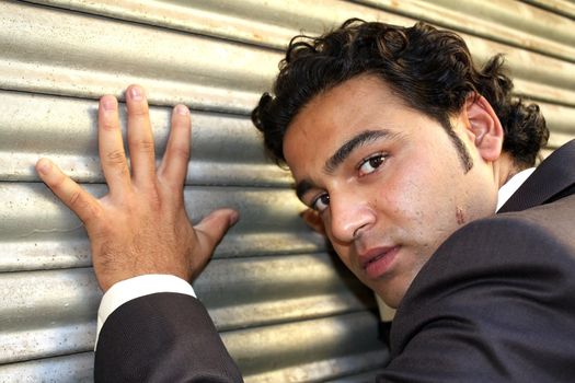 A portrait of a handsome Indian man near a shutter.