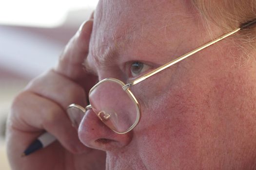 man with glasses on concentrating whilst holding a pen in his hand