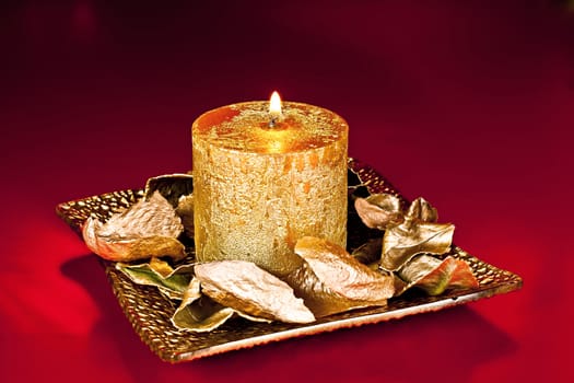 Richly decorated Christmas candle on the golden dish of golden petals ornament.