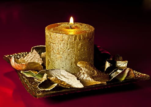 Richly decorated Christmas candle on the golden dish of golden petals ornament.
