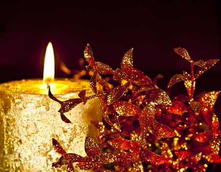 Christmas Decor, a burning candle with glossy leaves on a dark background.
