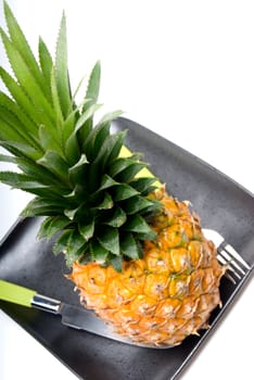 ripe pineapple on a black plate with knife and fork