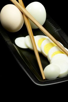 fresh boiled eggs one whole ,one peeled and another sliced on a black plate with chopstick