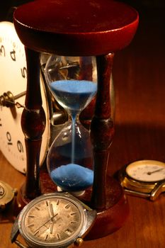 Hourglass, old watch and clock mechanism on wooden background