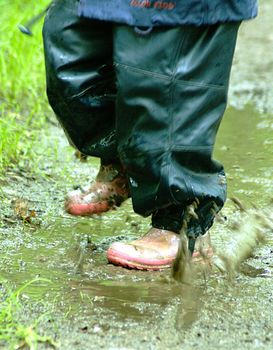 Closeup of two feet jumping on muddy road after rain.