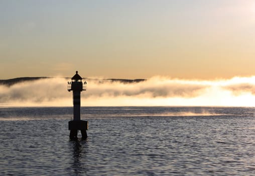 A lighthouse with mysterious mist approaching, illuminated by the evening sun.