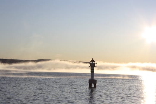 A lighthouse with mysterious mist approaching, illuminated by the daylight sun.