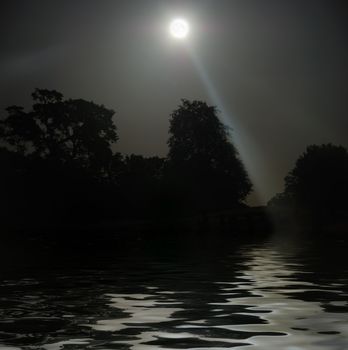 Full Moon shining above tree silhouettes and water.