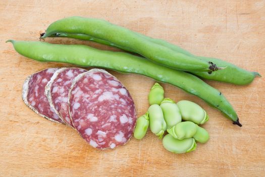 Three salami slices with fava beans on a wood chopping board