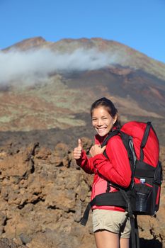 Healthy lifestyle concept- happy woman hiker giving thumbs up before the summit hike. Beautiful young Asian / Caucasian model. Image shows Pico Viejo from Teide National Park, Tenerife in the background with lots of copyspace.
