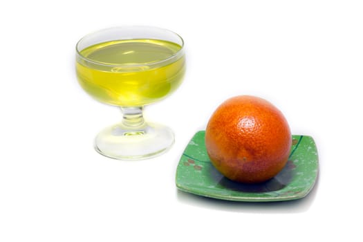 Yellow jelly but transparent glass and orange on green saucer on white background