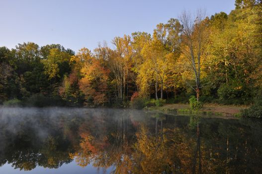 Morning mist on lake with trees turning autumn colors