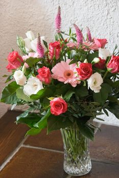 Glass vase with roses and gerberas in red, white and pink in afternoon sun