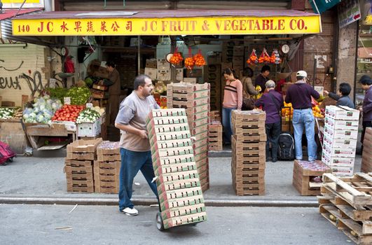 Man with hand truck of produce boxes in front of Chinese produce shop, chinatown, NYC