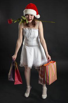 The amusing girl in a Christmas cap, with purchases and a rose