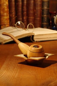 Still life with tobacco pipe lying on wooden table on background with old books and spectacles