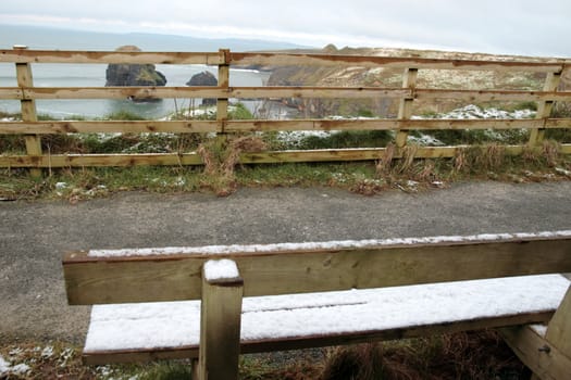 snow covered bench on the ballybunion cliffside walk in winter