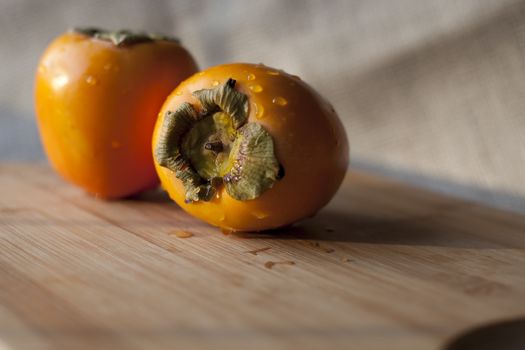 Fresh raw whole persimmons on cutting board with shallow depth of field.