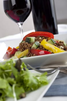 Lentil salad with wine in background and salad greens in foreground.  Vertical orientation.