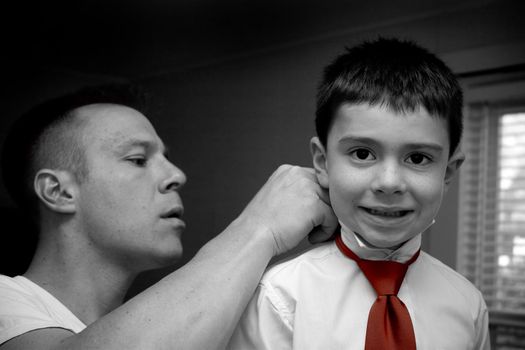 A groom helps his son get ready by putting on his tie.