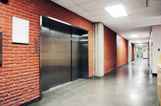 One freight stainless steel door elevator surrounded by brick wall of a deserted hallway. Could be office, school, retirement home and hospital.