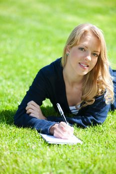 Pretty girl studying on a green meadow during summer