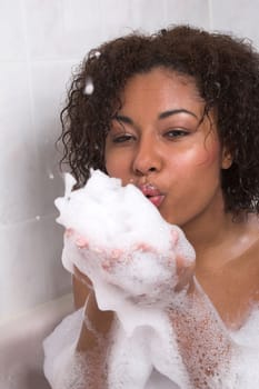 Beautiful black woman in a bathtub blowing bubbles