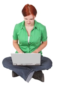 Redhead teenager sitting with her legs crossed and working on a laptop.