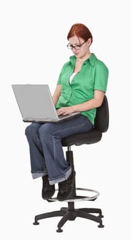 Redheaded teenager sitting on a high chair and working on a laptop.