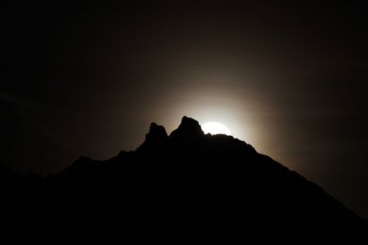 Moon shining bright behind black mountains