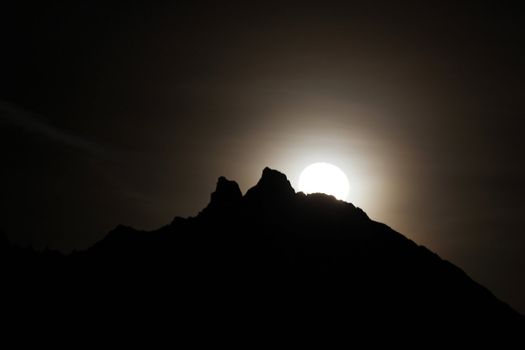 Moon shining bright behind black mountains