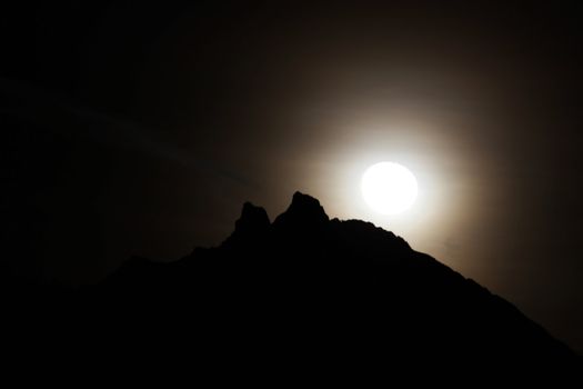 Moon shining bright behind black mountains