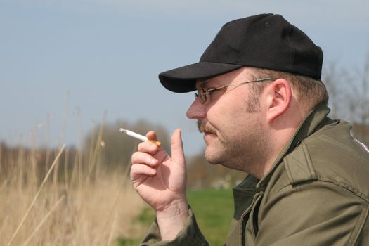 Fisherman sitting on the side of the water, smoking a cigarette while waiting for the fish to bite