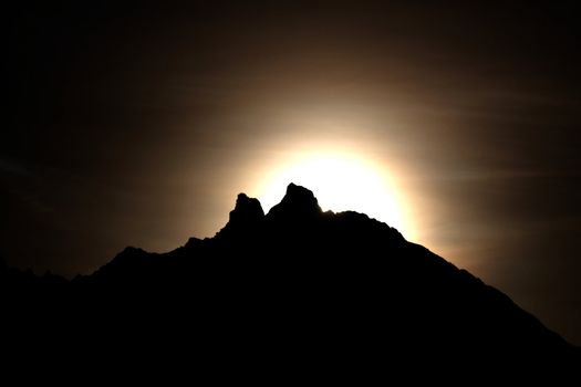 Moon shining bright behind black mountains