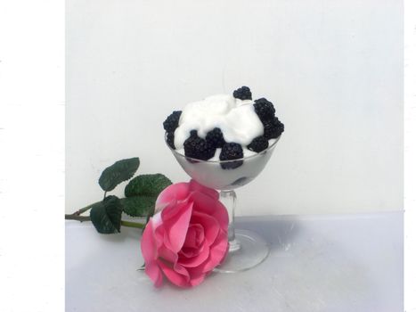 A glass full of yogurt and black berries and a pink rose on the side.