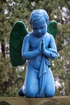 blue praying angel, blurred trees in background, photo taken in Presov, Slovakia