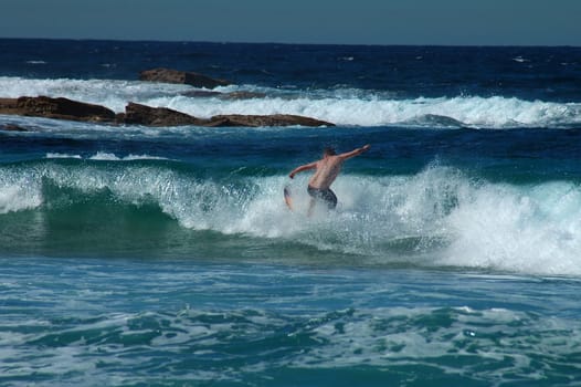 young man surfing on small wave, rocks in background, 