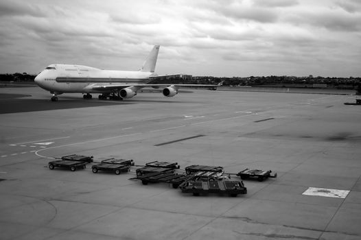 black and white photo of rolling airplane and luggage trolleys