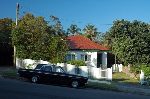 small white wooden house in suburb, black car parked in front