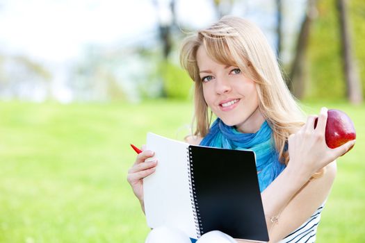 Pretty girl studying on a green meadow with notebook