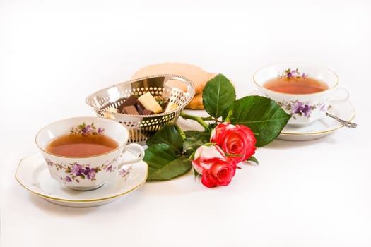 Two cups of tea with chocolates, cookies and red roses on white background