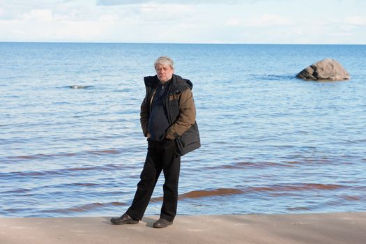 Mature man with grey hair relaxing at the Baltic sea in autumn day.