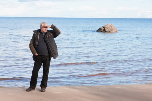 Mature man with grey hair relaxing at the Baltic sea in autumn day.