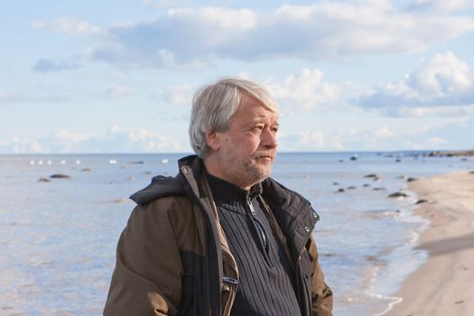 Portrait of mature concerned poor man with grey hair at the Baltic sea in autumn day.