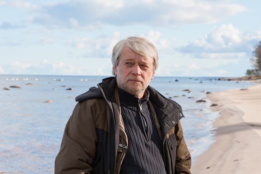 Portrait of mature thoughtful poor man with grey hair at the Baltic sea in autumn day.