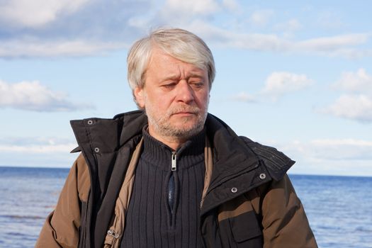 Portrait of mature thoughtful poor man with grey hair at the Baltic sea in autumn day.